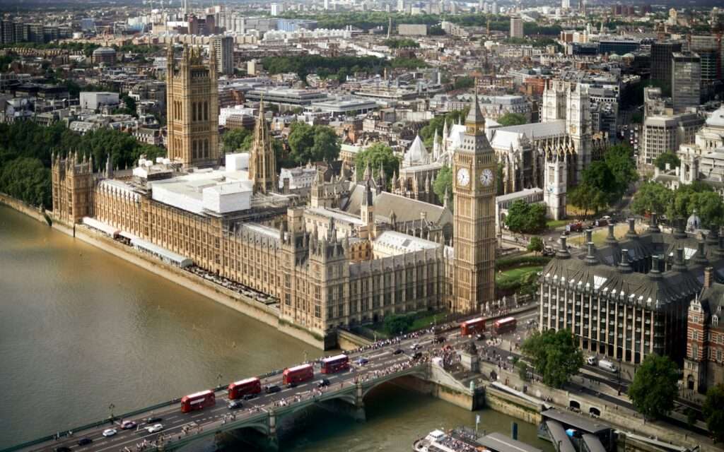 The Houses of Parliament and Big Ben from above, with red buses crossing Westminster Bridge